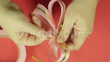 女人`<strong>双</strong>手伸直粉红色丝带礼物蝴蝶结的花瓣，给它蝴蝶结的形状。 <strong>红色背景</strong>